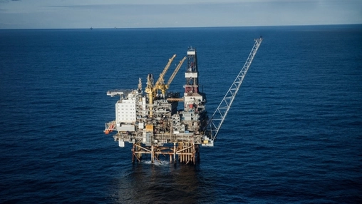 Aerial view of an offshore oil and gas platform with yellow cranes and accommodation modules on a calm sea