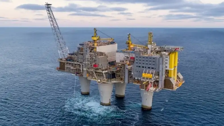 Large offshore oil and gas production platform with yellow crane structures on open sea under an overcast sky