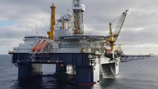 Offshore drilling platform with yellow derrick cranes and blue support columns operating in open grey waters