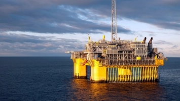 Large yellow offshore oil platform with full topside facilities in open sea at dusk