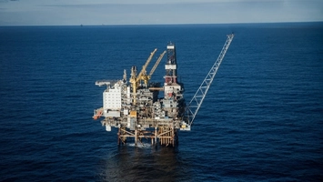 Aerial view of an offshore oil and gas platform with yellow cranes and accommodation modules on a calm sea