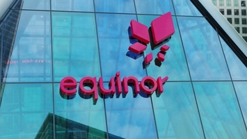 Pink Equinor logo and symbol on a glass building facade with office towers reflected in the glass panels